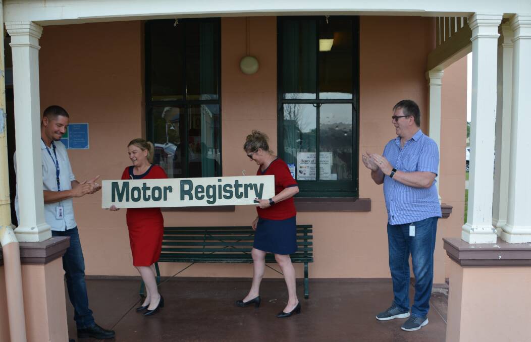 WE'RE OUTTA HERE: Katie Taylor and Barice Lewis cart off the old sign for the last Motor Registry in the state, taken down by (on left) Service NSW change and project lead Adrian Schmidt and transition manager Lewis Blume. Photo: Melinda Campbell.
