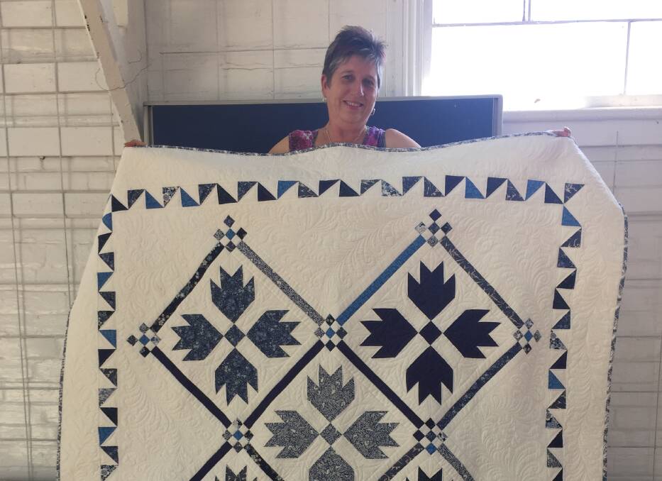 Tenterfield Arts and Craft Society president Fran Bulmer with this year's raffle quilt, now on display at Sullivan's Newsagency.
